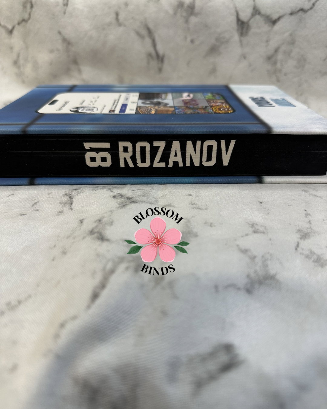 Book with '81 Rozanov' on a marble surface, featuring the 'Blossom Binds' logo.