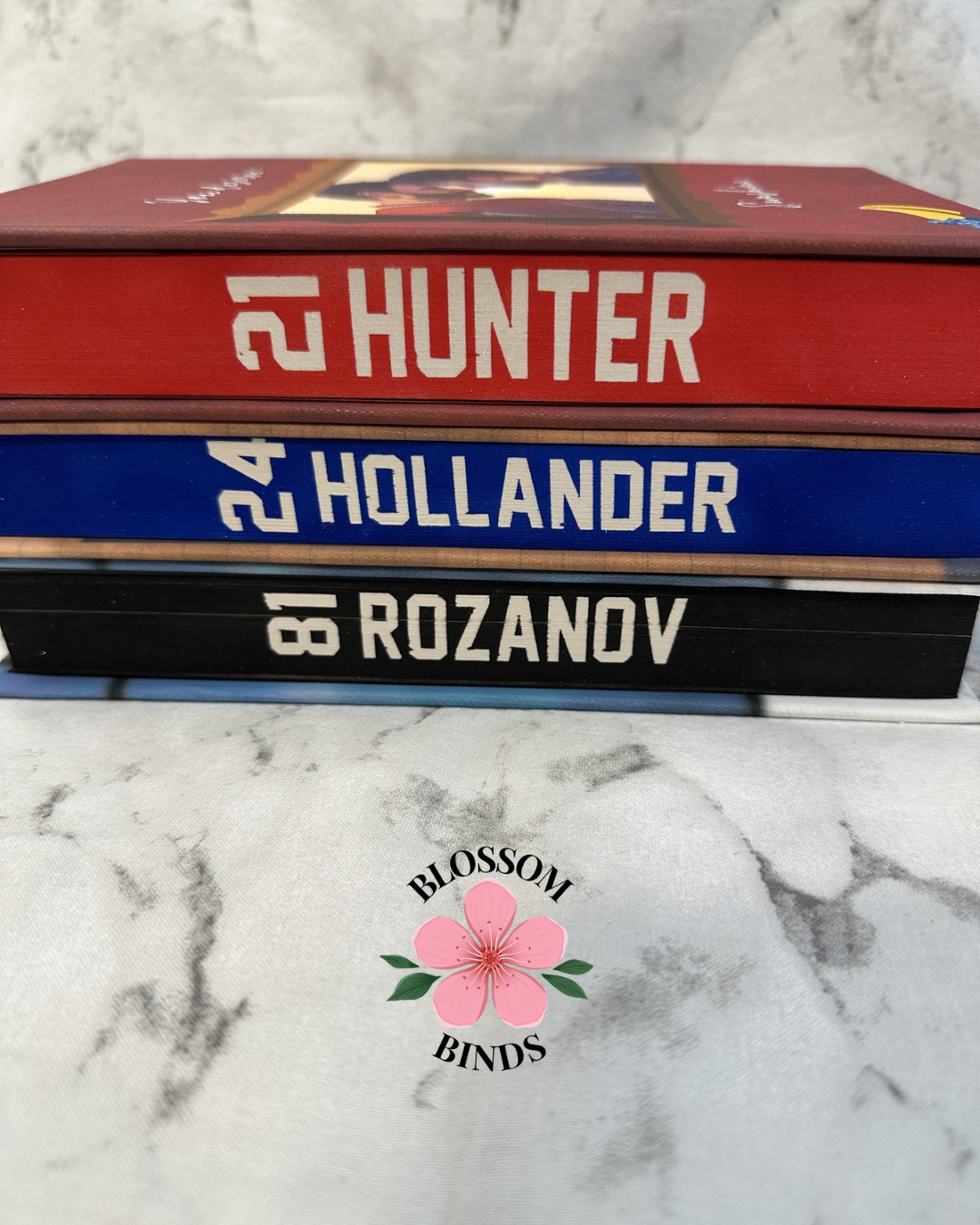 Stack of books with player names on a marble surface, featuring the 'Blossom Binds' logo.