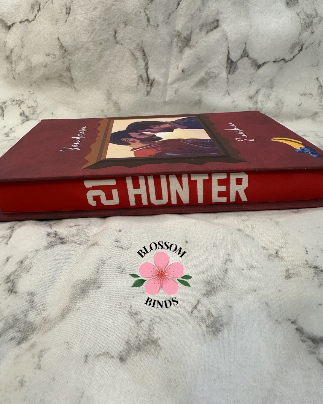 Red book with '21 Hunter' on a marble surface, featuring the 'Blossom Binds' logo.