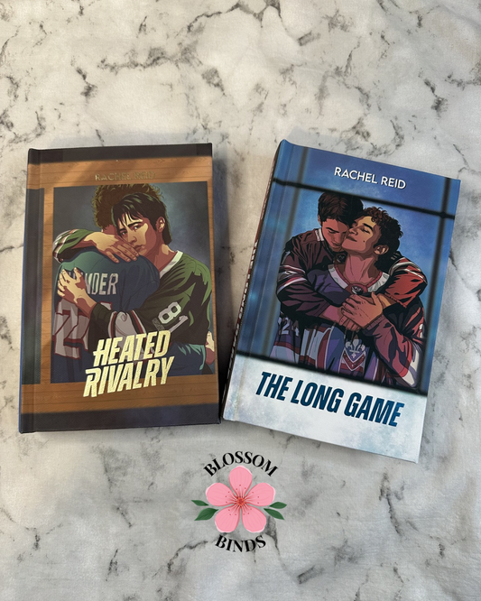 Two books titled 'Heated Rivalry' and 'The Long Game' by Rachel Reid on a marble surface with 'Blossom Binds' branding.