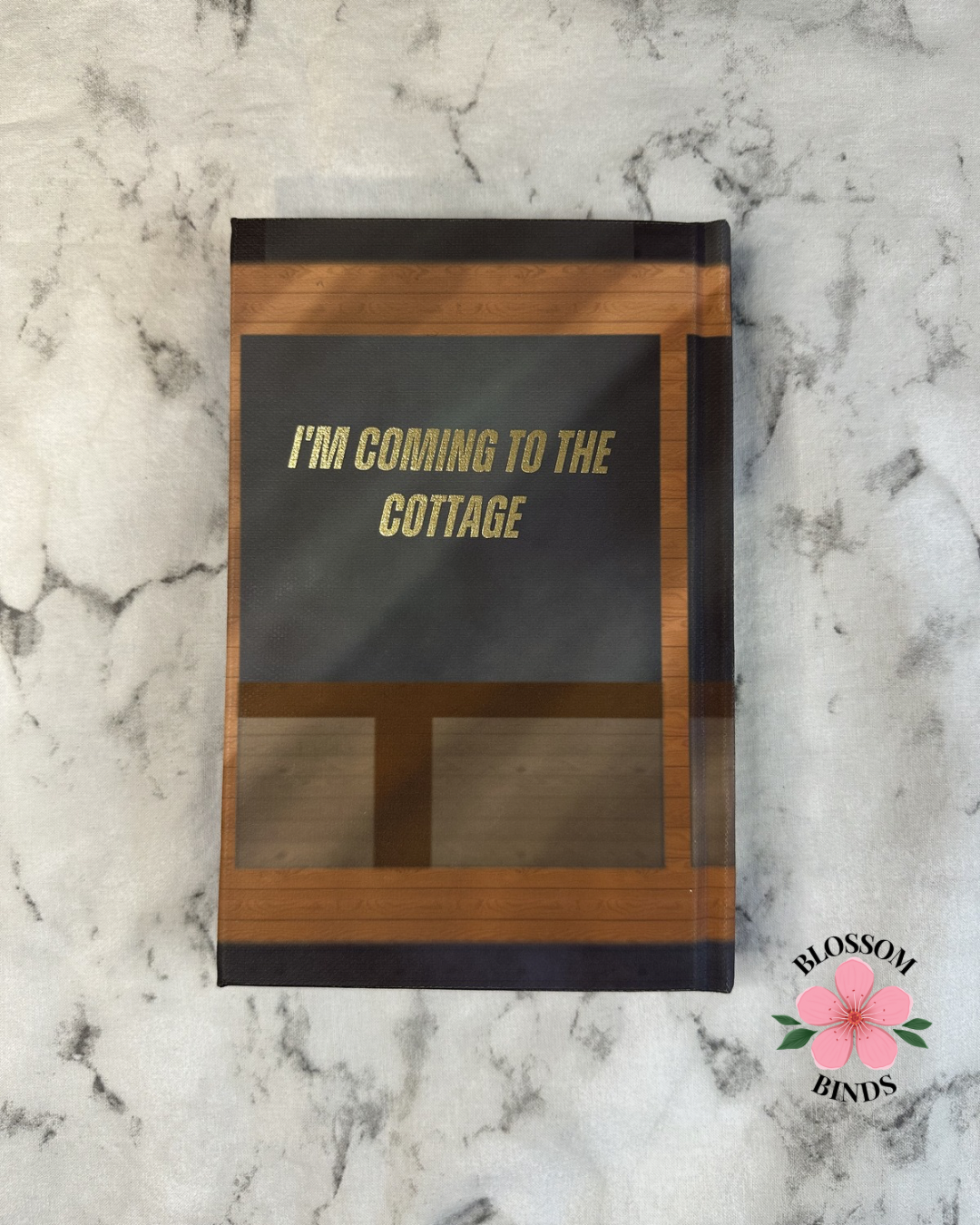 Book with 'I'm coming to the cottage' text on a marble surface, featuring the brand 'Blossom Binds'.