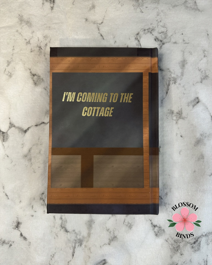 Book with 'I'm coming to the cottage' text on a marble surface, featuring the brand 'Blossom Binds'.