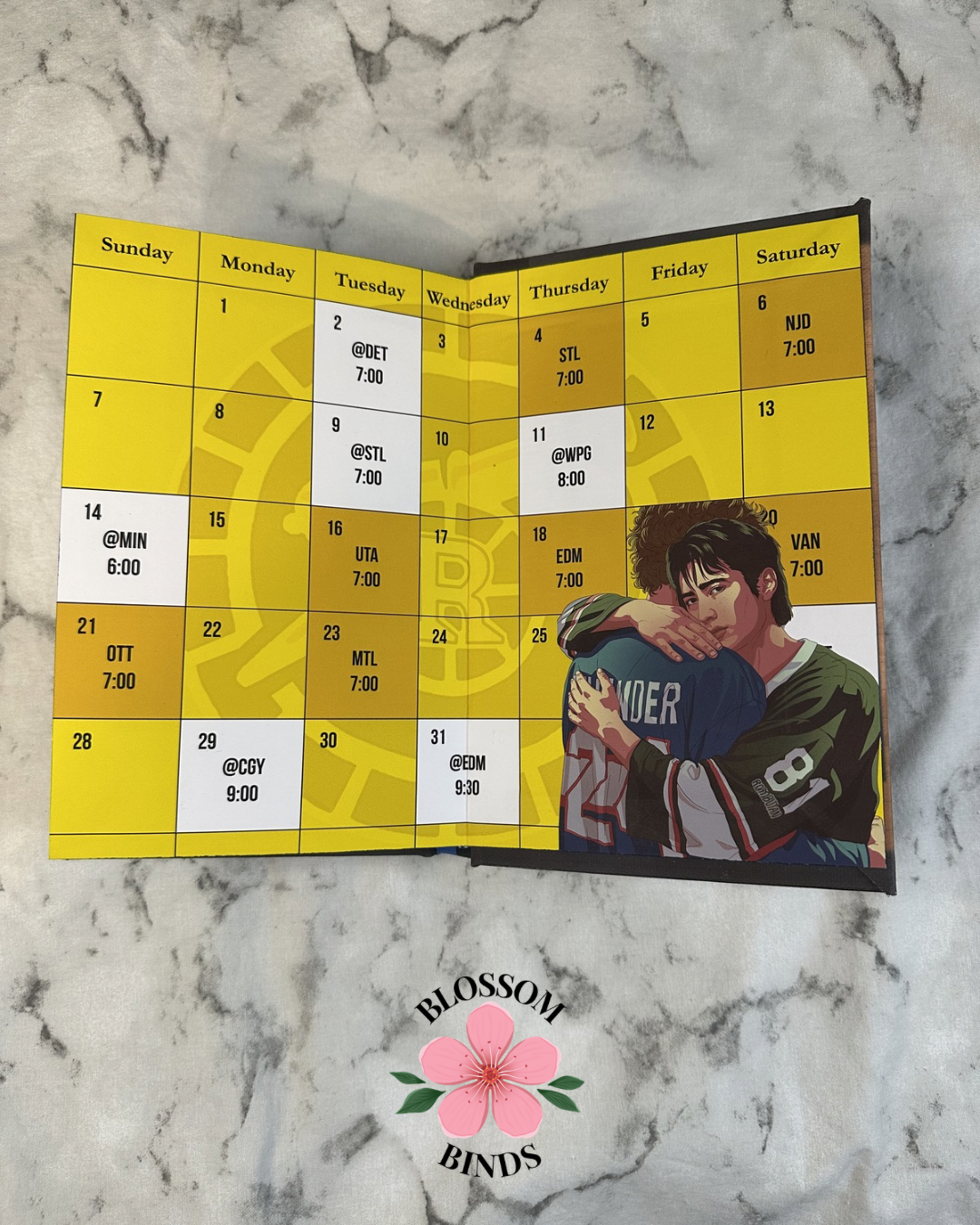 Calendar with a couple on a yellow background, placed on a marble surface with 'Blossom Binds' branding.