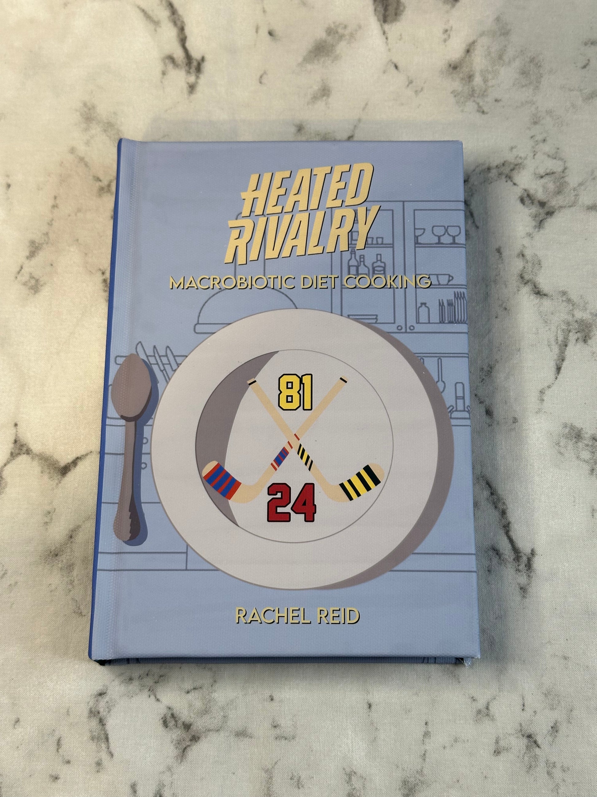 Book titled 'Heated Rivalry' by Rachel Reid on a marble surface